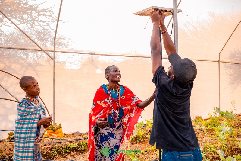 Women in the farm with an agritech expert installing an AI powered sensor, Farmshield. 